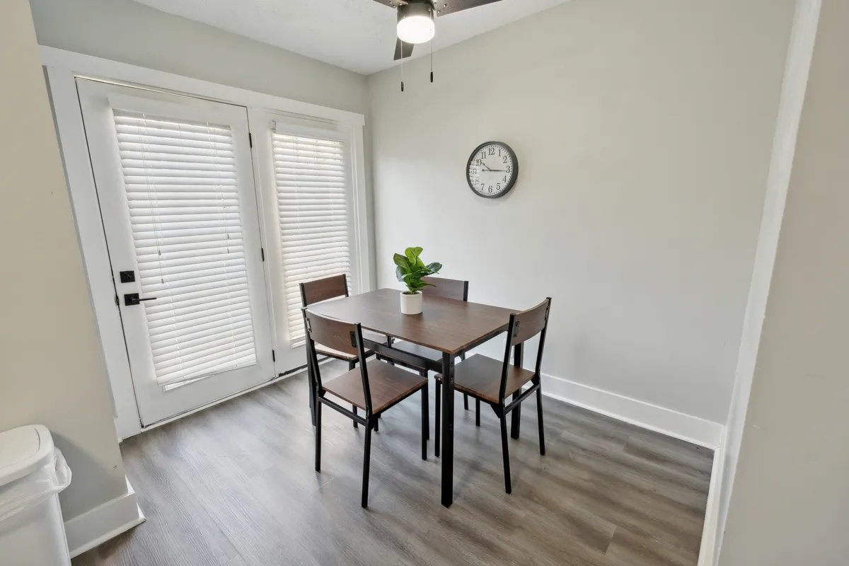 A dining area adjacent to the living space, featuring a sleek dining table, a vibrant plant, a wall clock, and glass sliding doors that let in plenty of sunlight. The room exudes a welcoming mood, ideal for casual meals, celebrations, or quiet coffee breaks, and visually connects communal and private moments within the home.