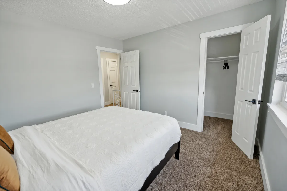 A cozy bedroom featuring a plush bed, a spacious closet, and a doorway leading into the rest of the home. The bedding looks inviting and soft, and the atmosphere is peaceful with subdued lighting and tidy organization.