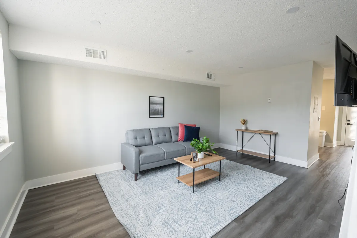 A modern living area with a gray sofa, wooden coffee table, decorative plants, and tasteful artwork on the wall. The space feels open and welcoming, with sunlight streaming in and a layout that encourages both conversation and relaxation, making it suitable for various activities from socializing to unwinding.