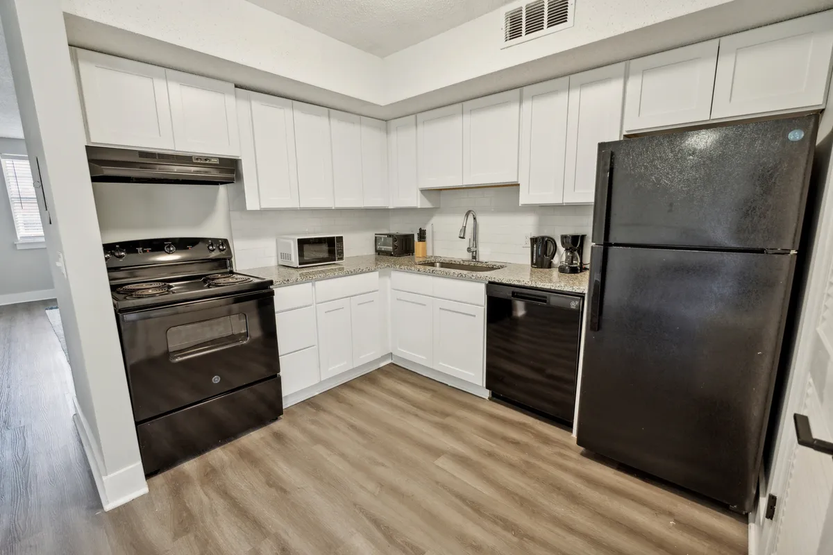 This image showcases a modern kitchen with black appliances, granite countertops, and crisp white cabinetry. The space is set up for both cooking and socializing, with surfaces and appliances inviting activity.