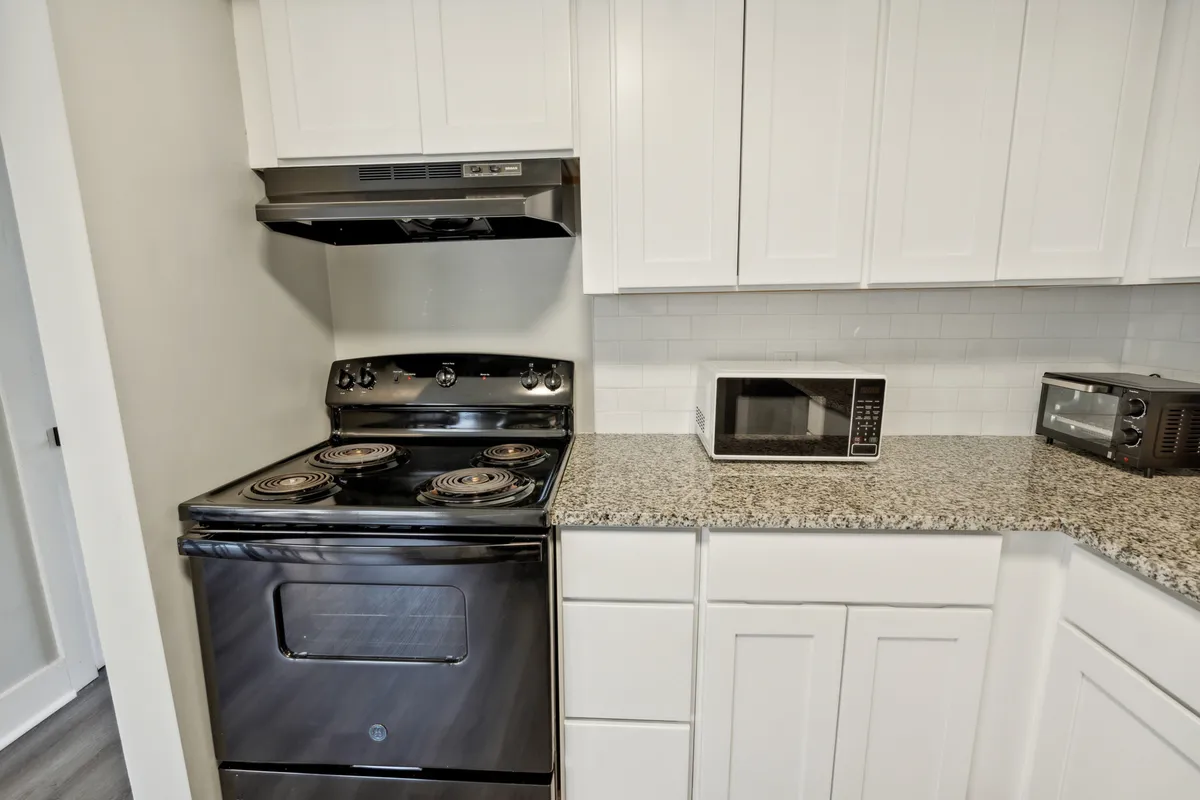 A close-up view of the kitchen focuses on a stylish black stove, granite countertops, and white cabinetry. The area is clearly arranged for both meal prep and entertaining guests.