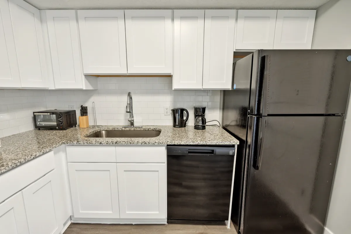 Here, the kitchen layout is highlighted with a granite countertop, black refrigerator, white cabinetry, and a sink. The scene hints at meal preparation and casual dining moments.